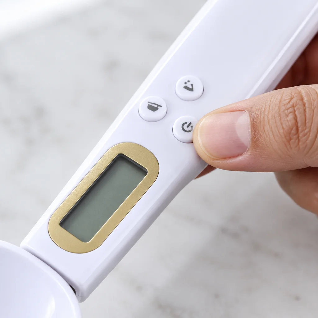 A macro photograph of the white Doseo digital weighing spoon’s three small molded buttons and the lo