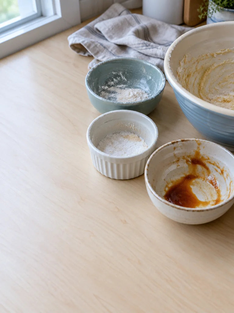 A close kitchen photograph of three small used prep dishes clustered around a mixing bowl, with trac